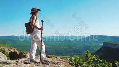 穿着牛仔帽和白色衣服的女旅行者站在山顶上，欣赏着令人惊叹的景色。
